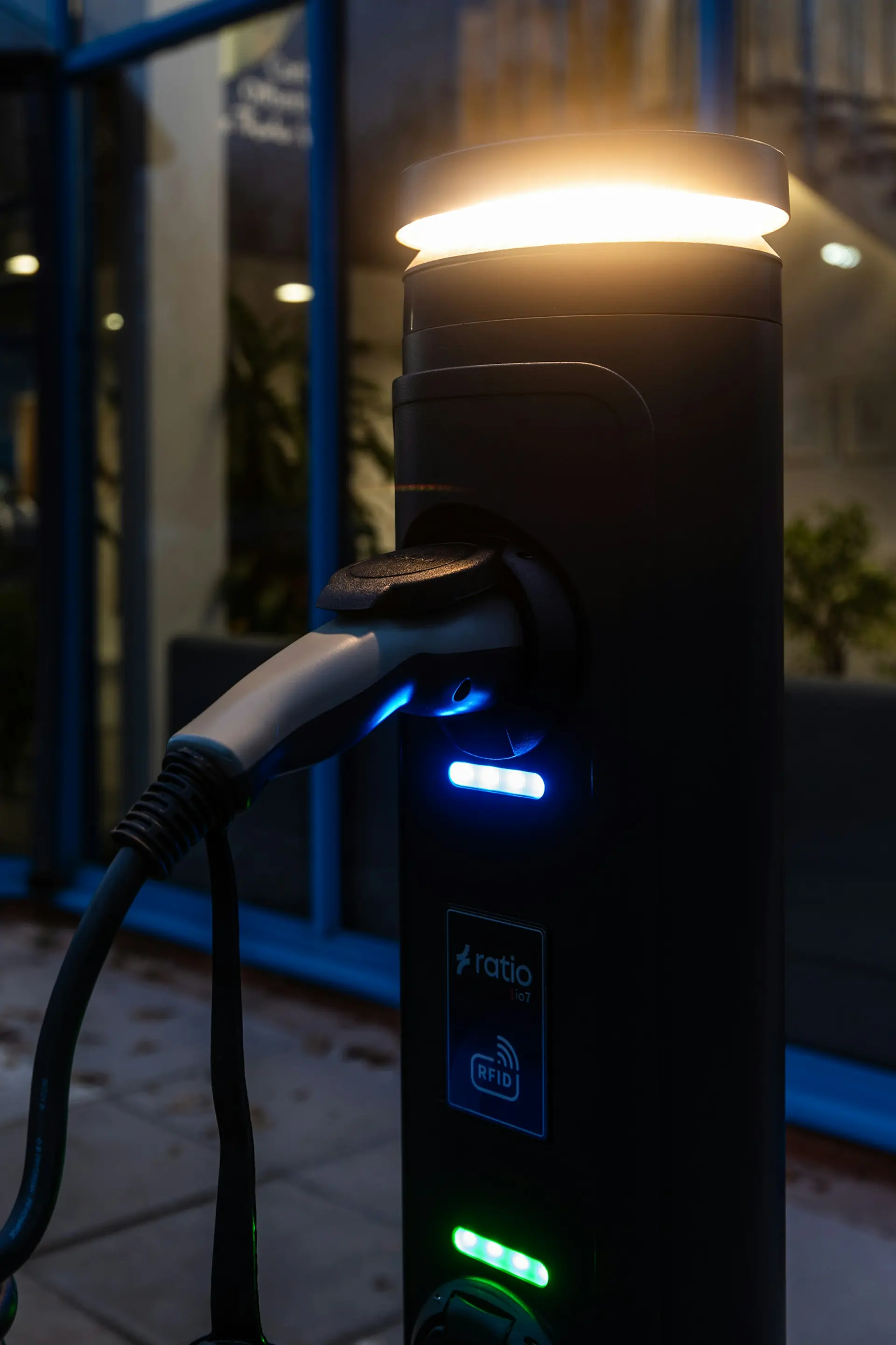 A charging post with its lamp lit, cable plugged in, at dusk